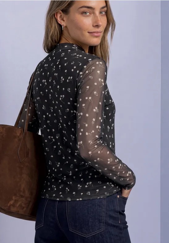 Eine Frau trägt ein schwarzes, transparentes, langärmeliges Blümchen-Shirt und eine braune Tasche über der Schulter.