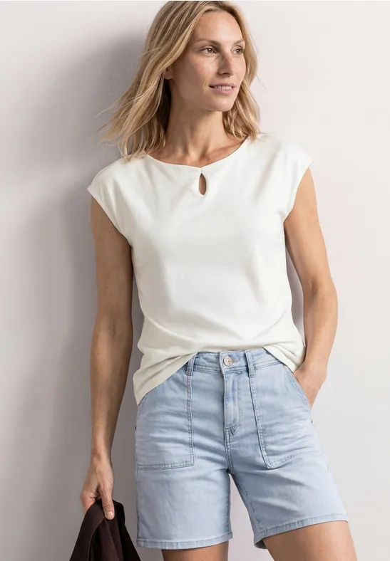 Frau in weißem T-Shirt und hellblauen Jeans-Shorts, legere Sommermode, Hände in den Taschen.