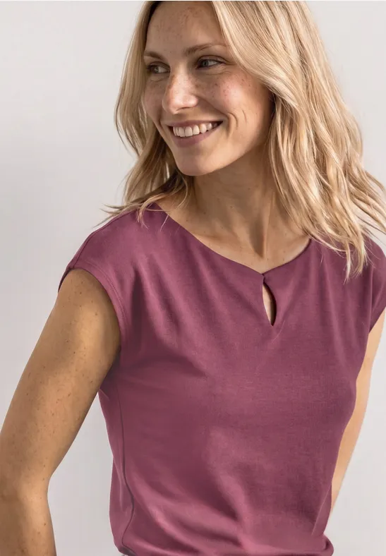 Femme aux cheveux blonds portant un haut sans manches rose devant un fond blanc.