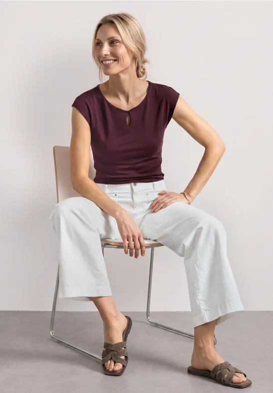 Femme assise sur chaise métallique, portant un top bordeaux, pantalon blanc ample et sandales plates