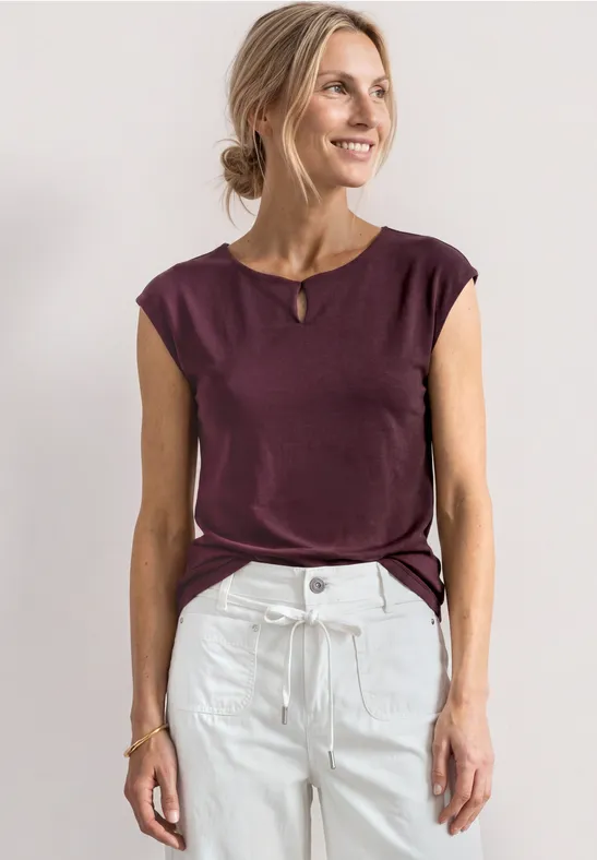 Femme en top bordeaux sans manches et jean taille haute blanc sur fond clair