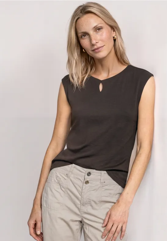 Femme portant un haut sans manches noir et un pantalon beige sur fond neutre.