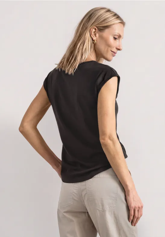 Femme portant un t-shirt noir et pantalon beige, vue de dos.