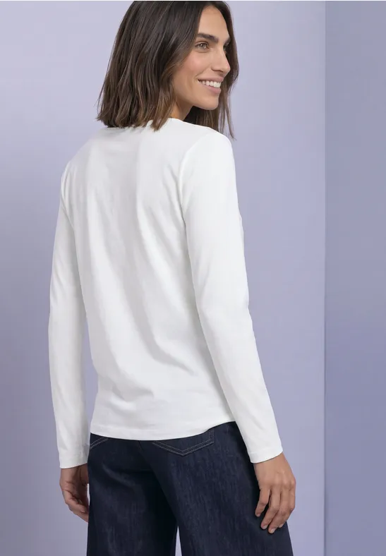 Frau von hinten in weißem Langarmshirt und dunkler Jeans vor fliederfarbenem Hintergrund.