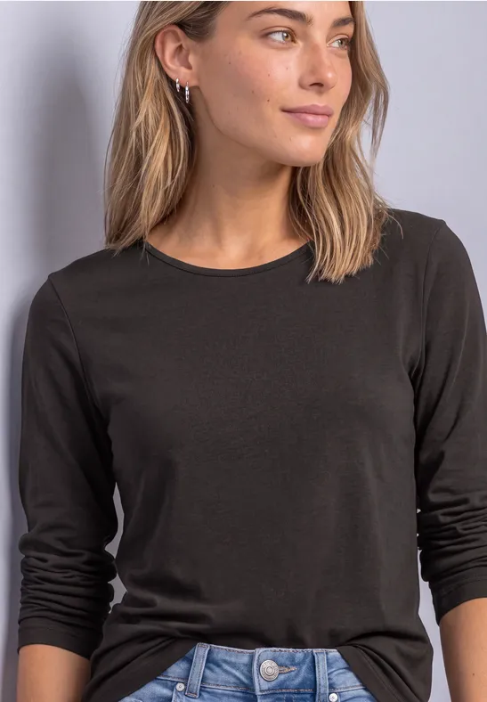 Une femme porte un t-shirt noir à manches longues sur un fond neutre.