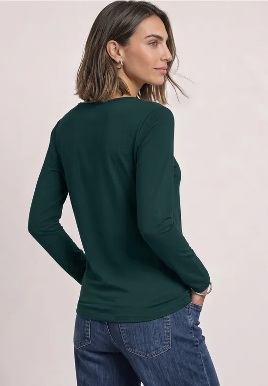 Frau von hinten mit dunkelgrünem Langarmshirt und Jeans vor hellem Hintergrund.