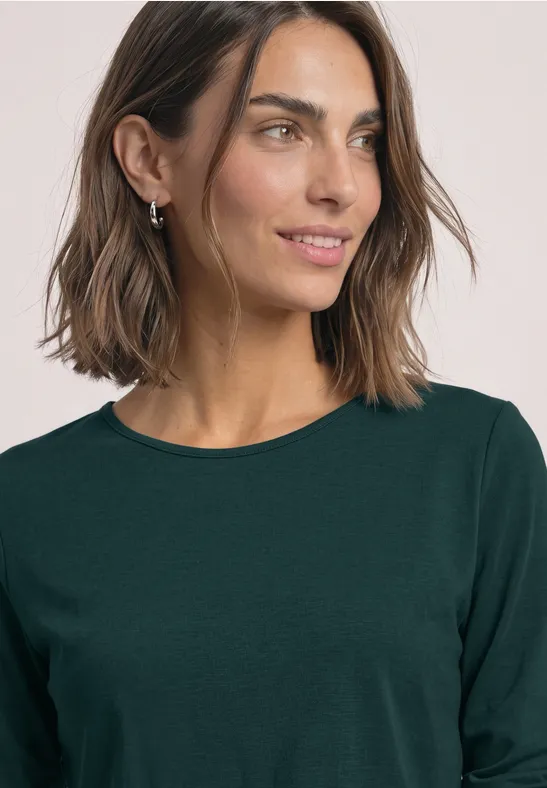 Frau mit schulterlangem braunen Haar und grünem Langarmshirt schaut lächelnd zur Seite.