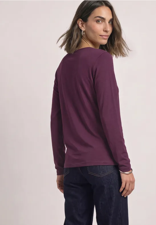 Frau in lila langärmligem Shirt und Jeans blickt über die Schulter.