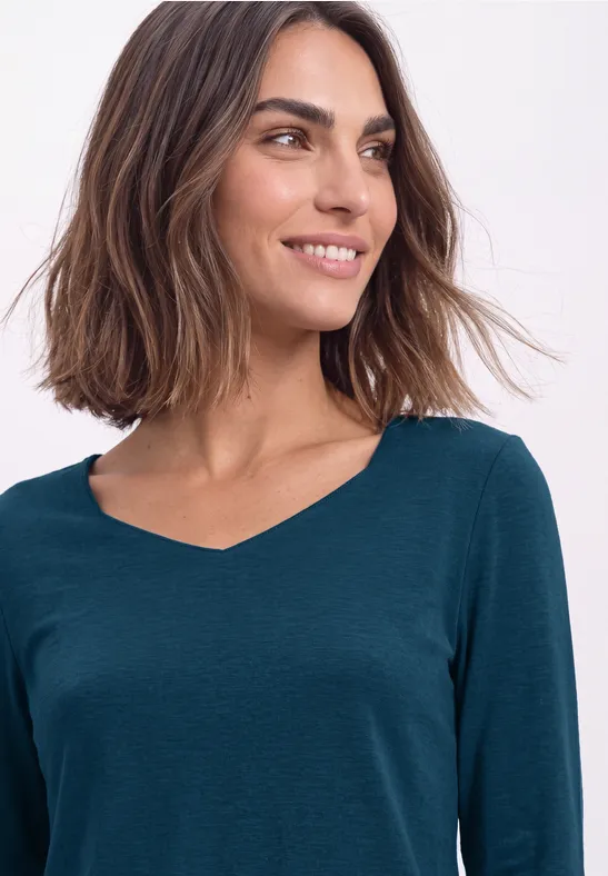 Frau mit schulterlangem braunem Haar und dunkelgrünem V-Ausschnitt-Shirt lächelt seitlich.