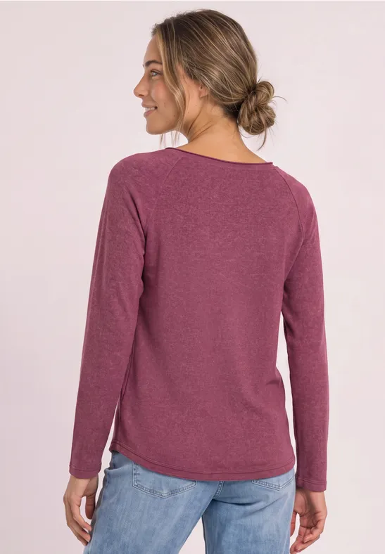 Frau von hinten in einem langärmligen bordeauxroten Pullover und blauen Jeans.