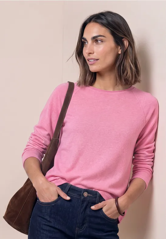 Femme portant un pull rose et un jean bleu avec un sac à bandoulière marron sur fond beige.