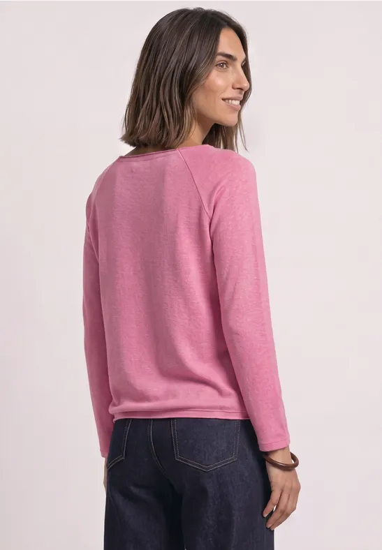Une femme en pull rose et jean bleu regarde par-dessus son épaule.