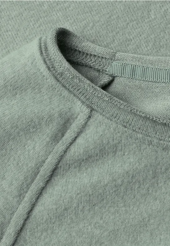 Gros plan d’un t-shirt vert menthe à col rond et couture apparente.