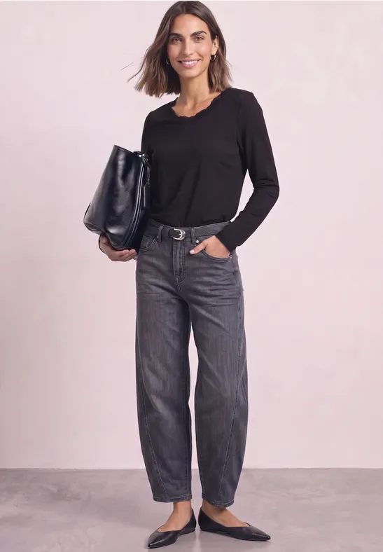 Frau in schwarzem Langarmshirt, weiten Jeans und schwarzen Ballerinas mit großer schwarzer Tasche vor hellem Hintergrund
