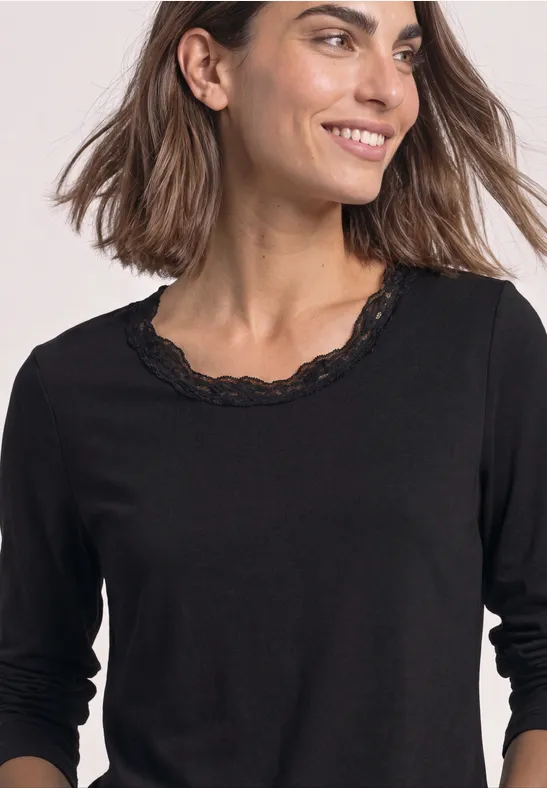 Frau trägt schwarzen 3/4-Arm-Pullover mit Spitzenbesatz am Rundhalsausschnitt.