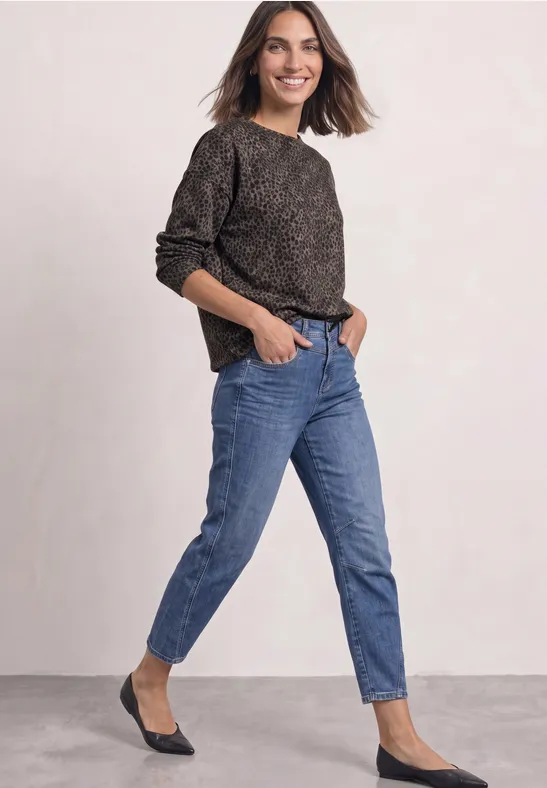 Femme portant un pull noir décontracté, un jean bleu et des ballerines noires.