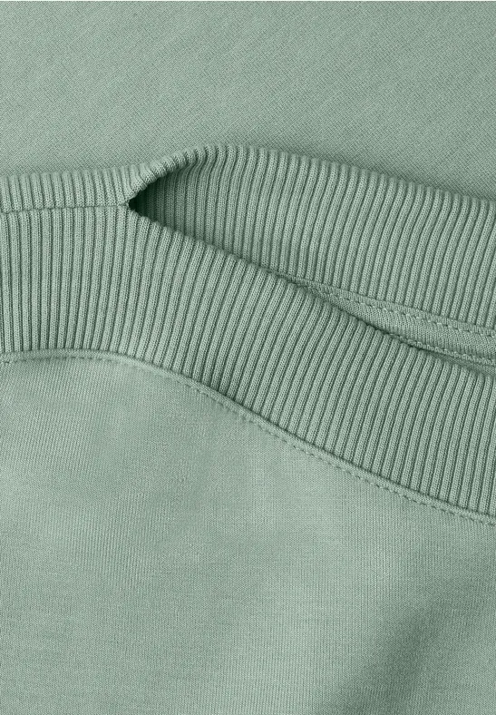 Close-up van een saliegroen sweatshirt met geribbeld boord en zichtbare stiknaad.