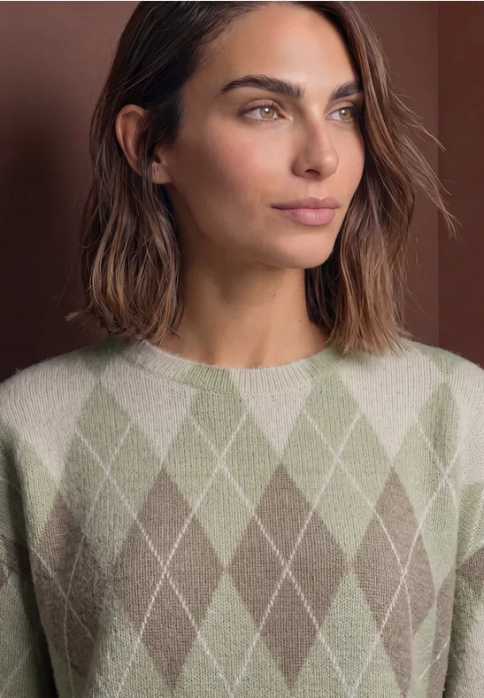 Femme aux cheveux bruns mi-longs portant un pull vert pâle à motif losange, fond sobre.
