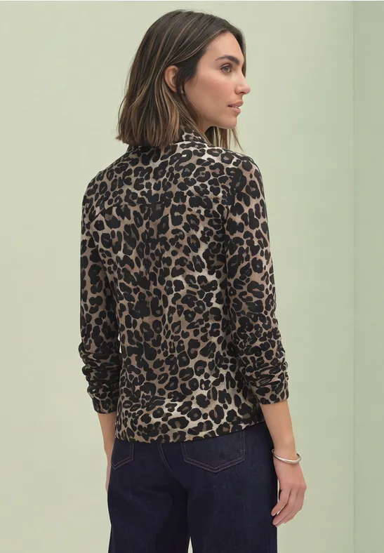 Frau von hinten in leo-print Langarmshirt und dunkler Hose vor neutralem Hintergrund.