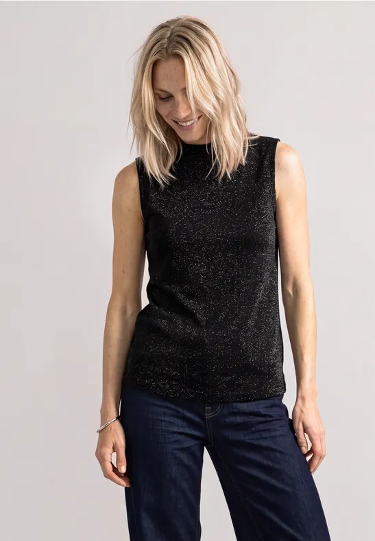 Une femme porte un haut noir pailleté et un jean bleu.