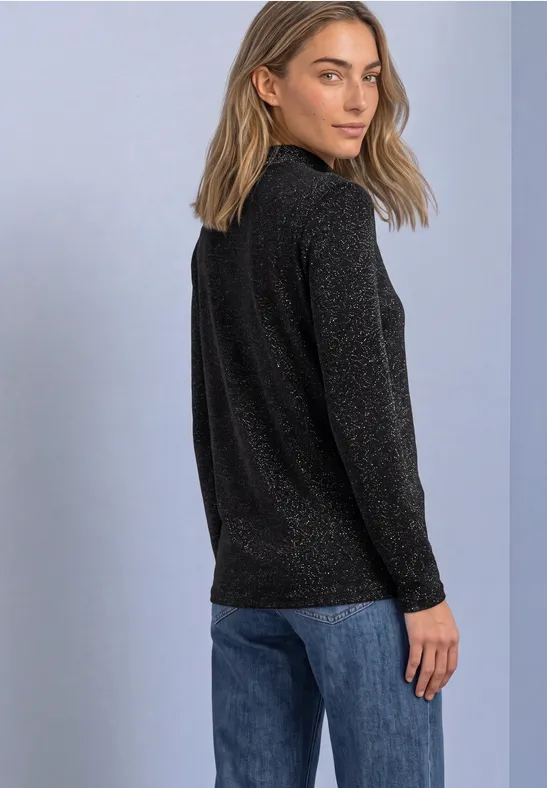 Femme vêtue d’un pull noir pailleté et de jean bleu, regard par-dessus l’épaule.