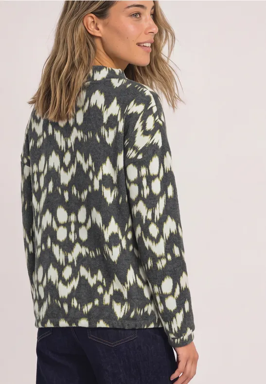 Une femme porte un pull vert et blanc à motif ikat et regarde par-dessus son épaule.