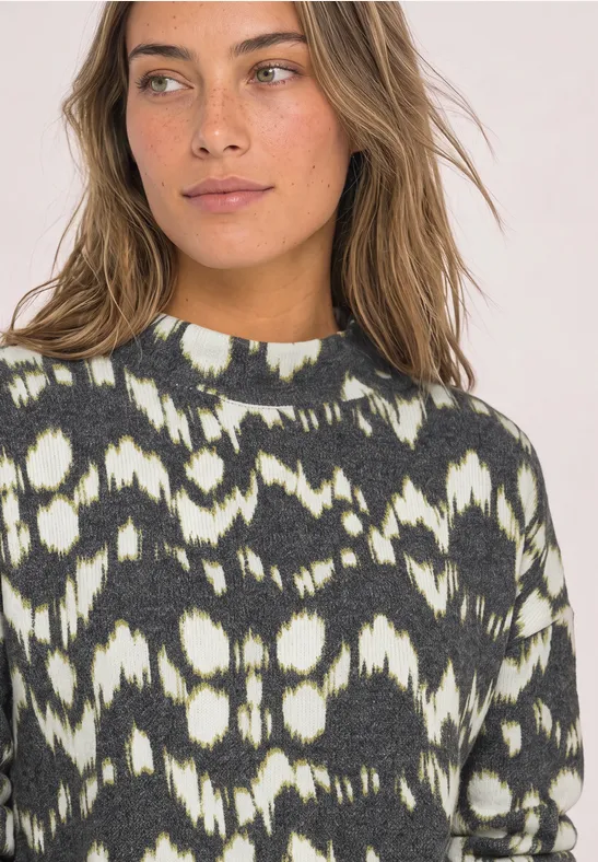 Une femme porte un pull noir et blanc à motif abstrait en regardant sur le côté.