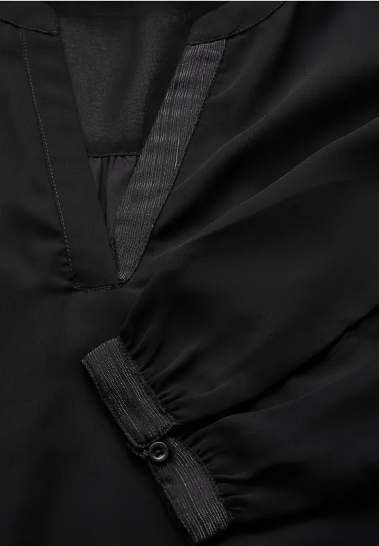 Detail einer schwarzen Bluse mit V-Ausschnitt und Manschette.