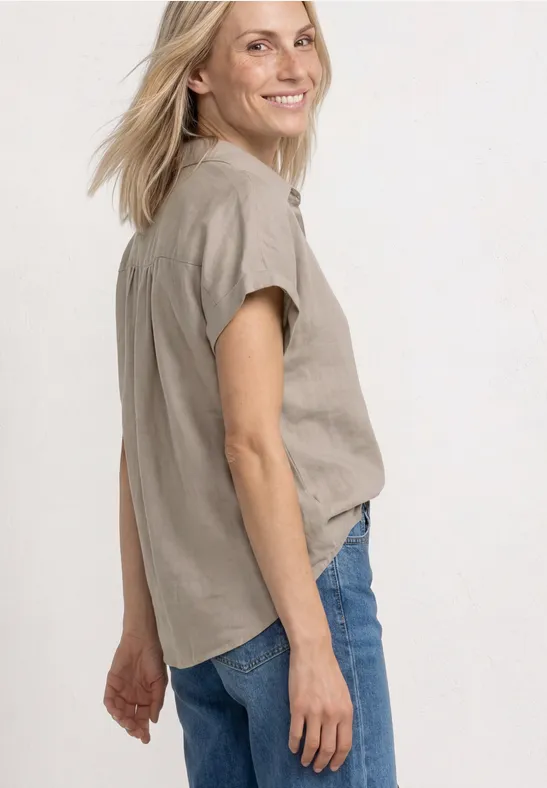 Vrouw in profiel met beige blouse en blauwe spijkerbroek.