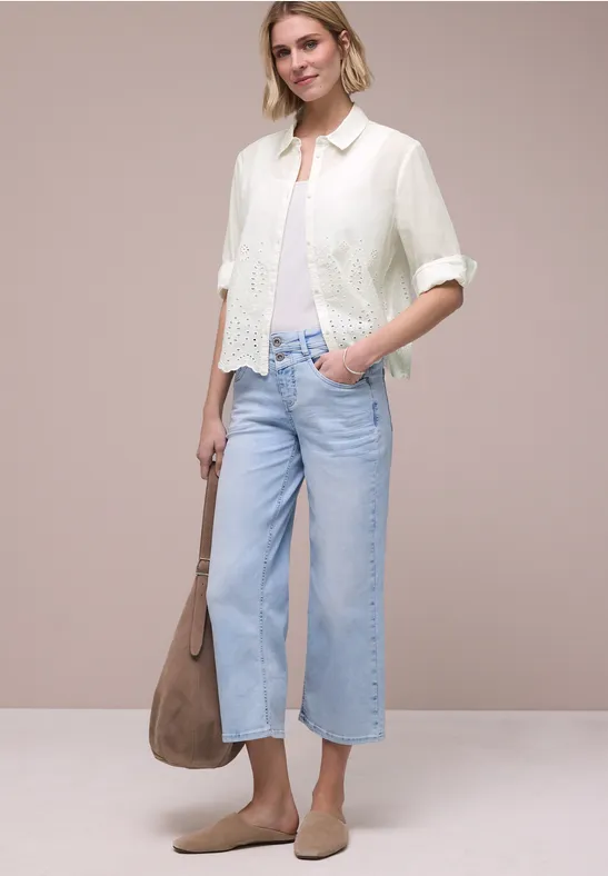 Vrouw in witte kanten blouse, lichtblauwe wijde cropped jeans, beige loafers en grote lichtbruine tas.