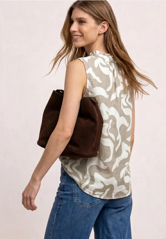 Femme de profil portant un top beige à motif floral, un jean bleu et un sac en daim marron sur l'épaule.