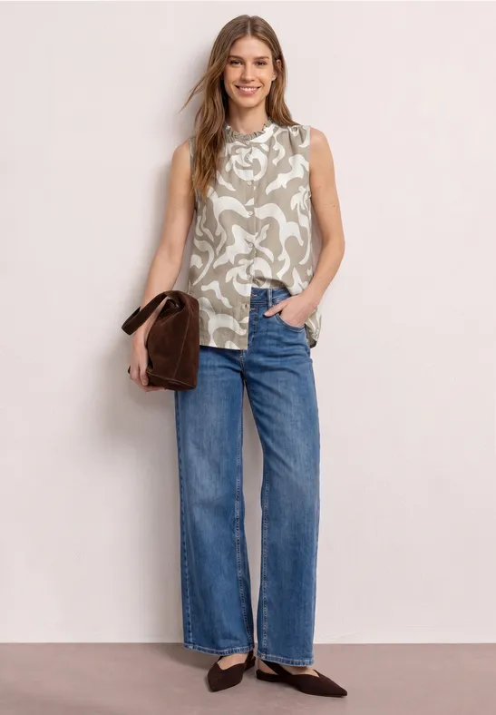 Femme en top sans manches à motifs, jean droit, ballerines noires et sac marron.