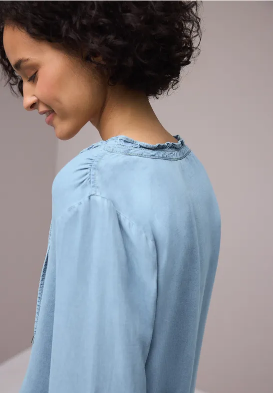 Zijaanzicht van een persoon met donker krullend haar in een lichtblauwe spijkerblouse.