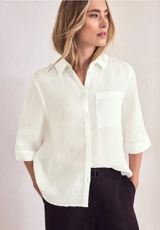Vrouw in wit linnen overhemd met borstzak en zwarte broek, casual met opgerolde mouwen.