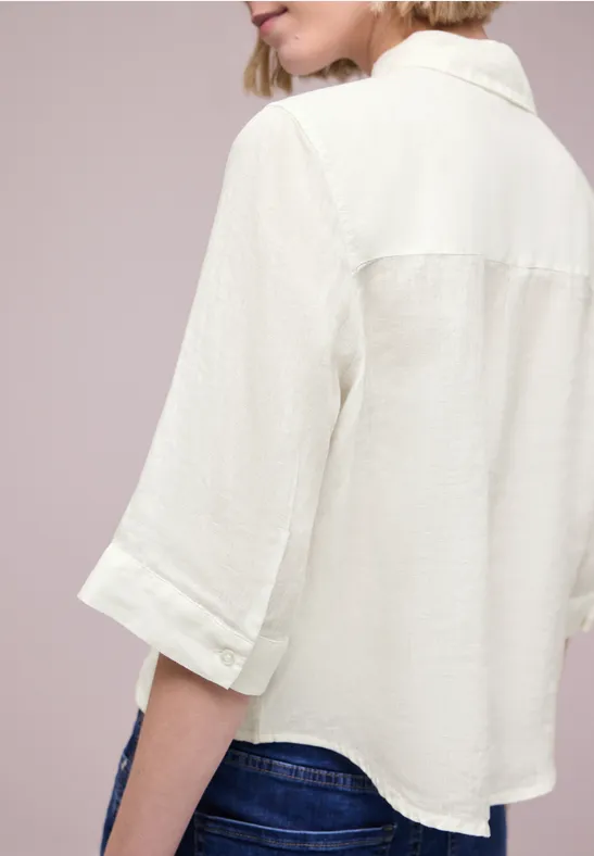 Achteraanzicht van een persoon in een losse crème blouse met driekwartmouwen en een blauwe spijkerbroek.