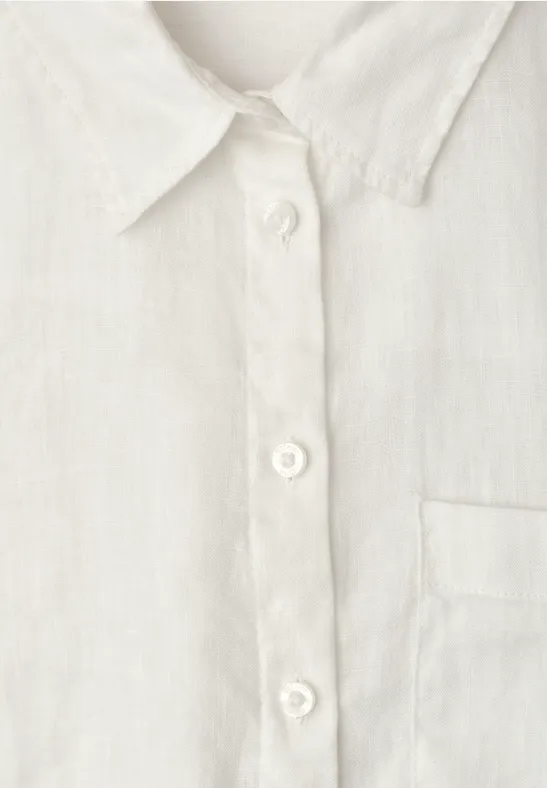 Close-up van een witte blouse met knoopsluiting en borstzak.