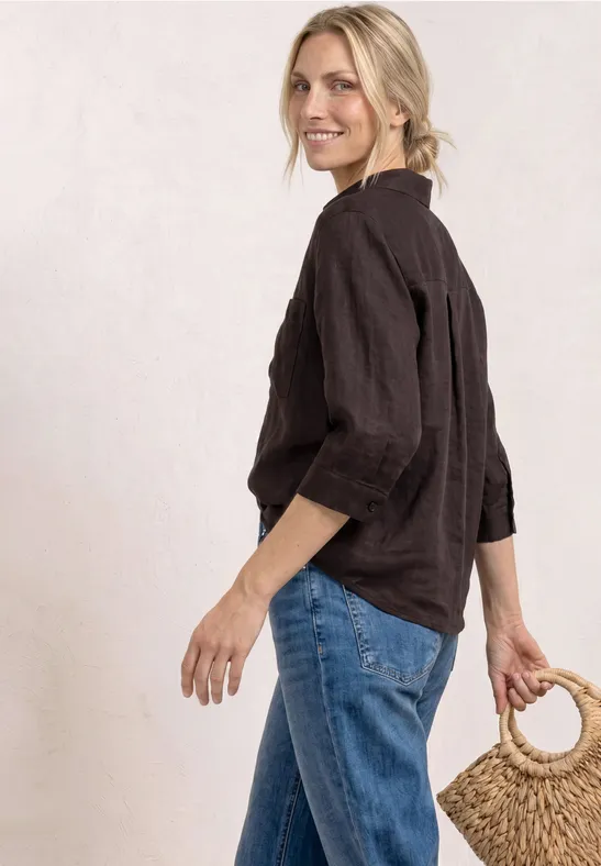 Blonde vrouw met zwarte linnen top en blauwe jeans, zijwaarts staand en houdt een gevlochten mandhengsel vast.