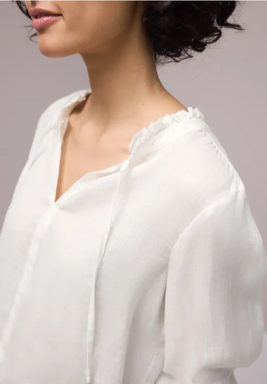 Eine Frau im Profil trägt eine weiße, luftige Bluse mit V-Ausschnitt und locker fallenden Ärmeln.