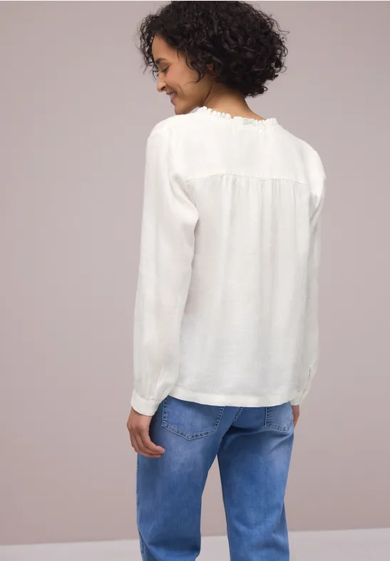 Frau von hinten in weißer Bluse und blauen Jeans vor neutralem Hintergrund.