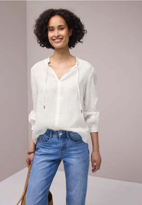 Frau in weißer Bluse und Jeans vor neutralem Hintergrund