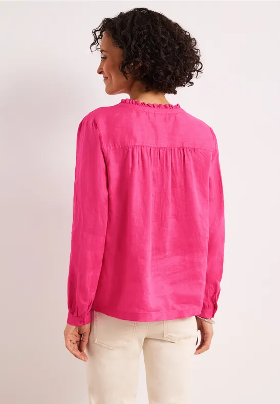 Vrouw van achteren met krullend haar, in een felroze blouse en lichte broek.