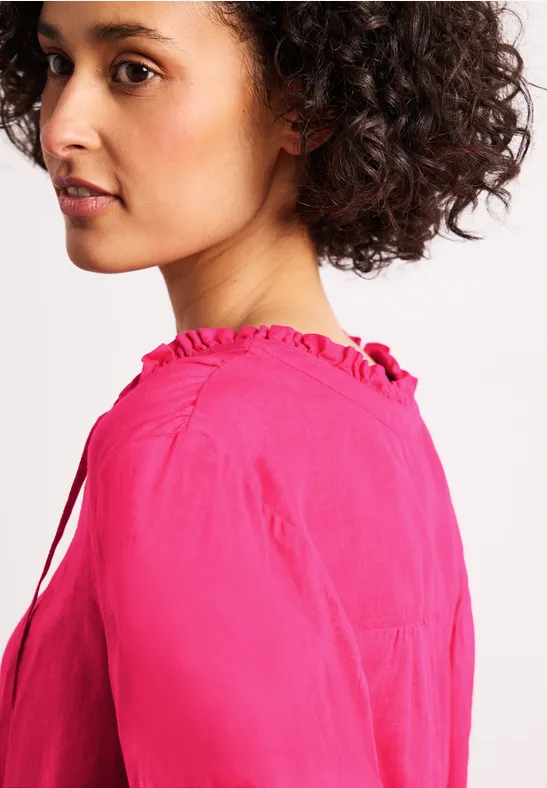 Zijaanzicht van een persoon met krullend haar in een felroze blouse. Gezicht wazig.