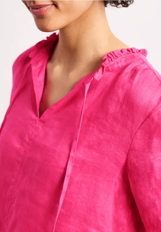 Een persoon draagt een felroze linnen blouse met V-hals en gerimpelde kraag.