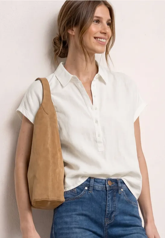 Eine Frau trägt eine weiße Kurzarmbluse, blaue Jeans und eine beige Schultertasche.