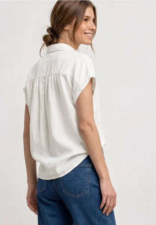 Person von hinten mit weißem Kurzarmhemd und blauen Jeans, Haare zum lockeren Dutt gebunden.