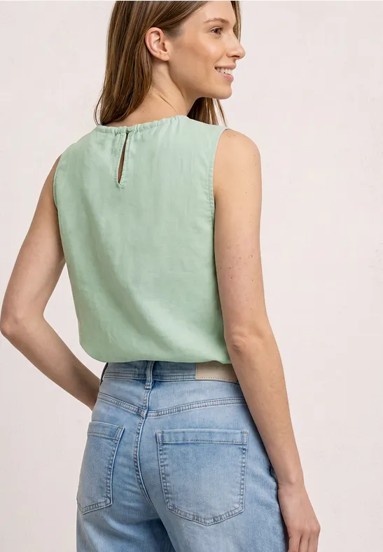 Een vrouw van achteren draagt een mouwloze mintgroene top en een lichte spijkerbroek.