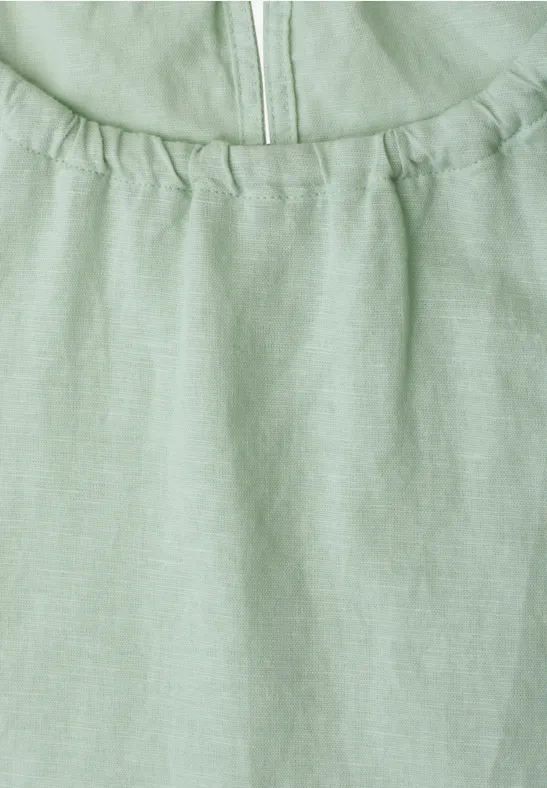 Close-up van een lichtgroen linnen top met rimpels bij de halslijn en een ritssluiting