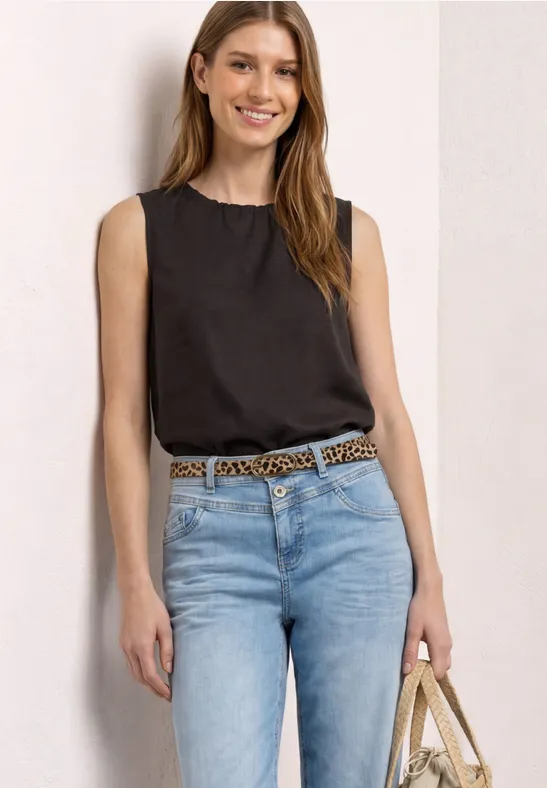 Vrouw met zwart mouwloos topje, lichte spijkerbroek, luipaardriem en strooien tas.