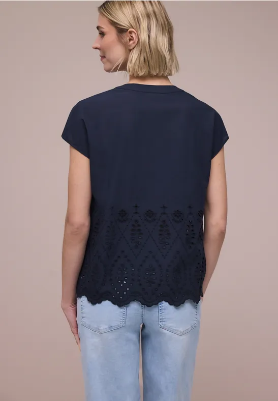 Frau von hinten in dunkelblauem kurzärmligem Top mit Spitzenbesatz am Saum und hellen Jeans.