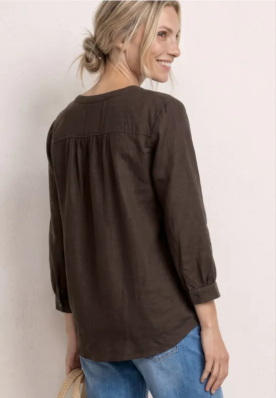 Achteraanzicht van een vrouw in een bruine blouse en spijkerbroek tegen lichte achtergrond.